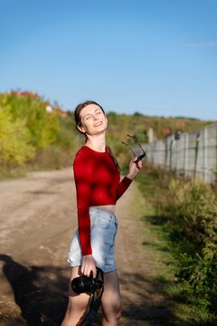 Person walks along a dirt path on a sunny day holding a camera and sunglasses