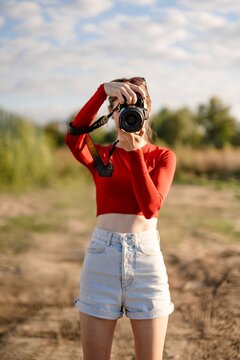 Woman holding camera in a field during daylight with blue sky and clouds