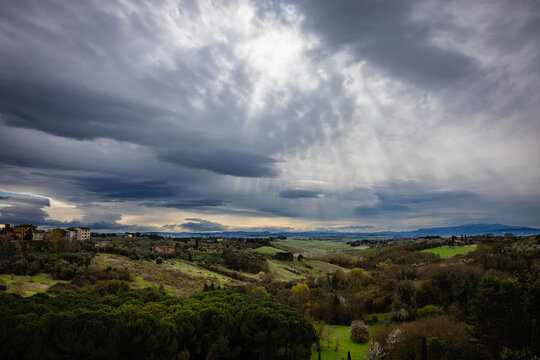 Sun rays breaking through dramatic clouds over Tuscan hills