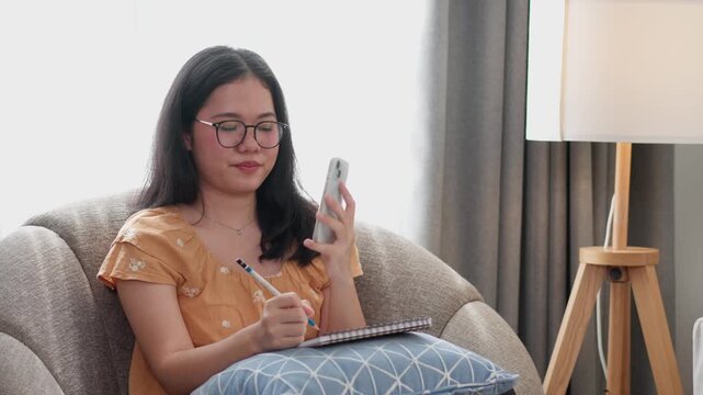 A young woman talks on a smartphone while sitting on a sofa at home, representing personal communication and modern digital lifestyle. Suitable for communication, social media, mobile technology