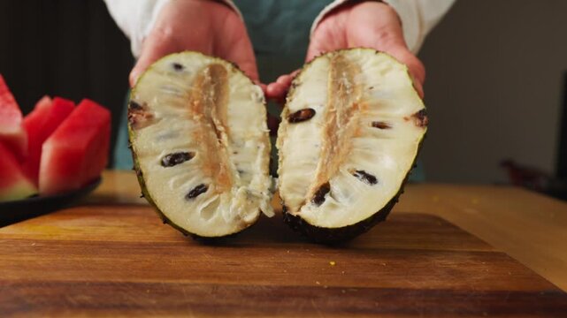 Hands holding a fresh soursop cut in half on a wooden cutting board