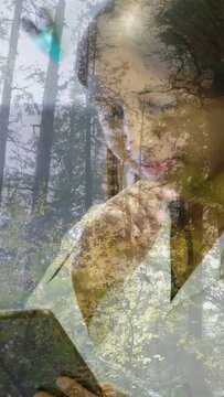 Vertical video: Woman glancing, tapping screen, touching chin and studying tech with forest overlay