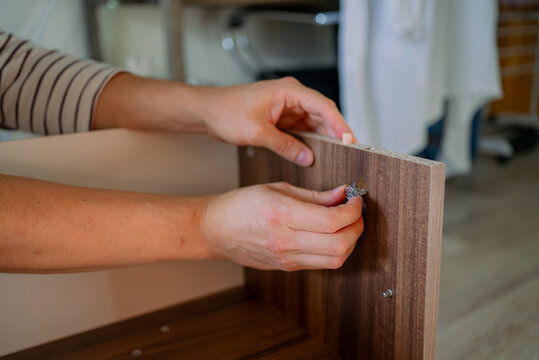Person's hands meticulously assembling a wooden flat pack tv stand, inserting a cam lock into a pre drilled hole, demonstrating the process of home improvement and furniture construction