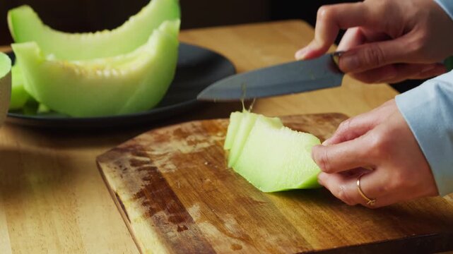 Cutting fresh honeydew melon into slices on a wooden cutting board