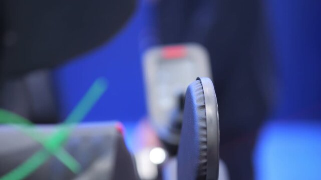 Close-up of gaming chair and controller in use. Person's hand grips controller. Background shows blurred gaming setup and lights. Focus on chair's headrest and armrest detail
