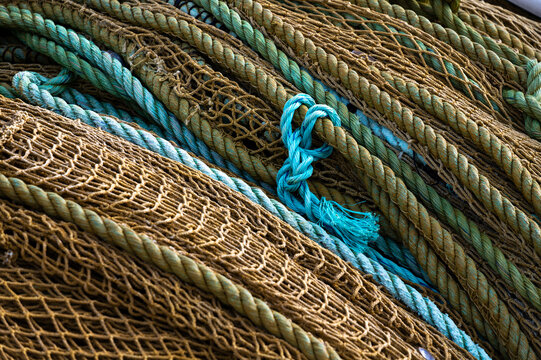 Close-up of old and weathered fishing nets and ropes featuring distinctive knots, varied textures and turquoise elements used in traditional fishing.