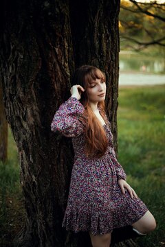 Woman leans against a tree by the lake during sunset in a natural setting