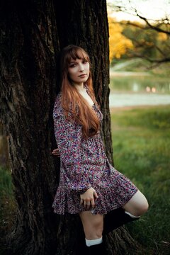 Woman leans against a tree by the lake during sunset in a natural setting