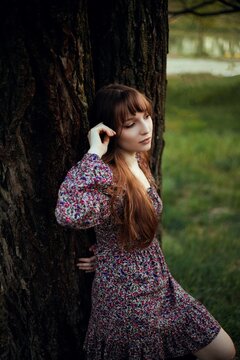 Woman leans against a tree by the lake during sunset in a natural setting