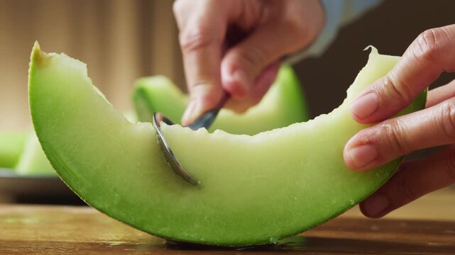 Hands scooping green honeydew melon flesh with a spoon