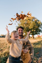 Obraz premium Happy father with two children tossing autumn leaves outdoors on a countryside walk for seasonal background