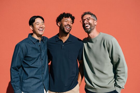 Three men laughing together against a coral wall background for social media and team lifestyle portraits