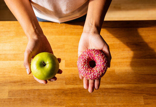 Hands holding green Generic Object and pink glazed donut with sprinkles over wood table healthy versus unhealthy