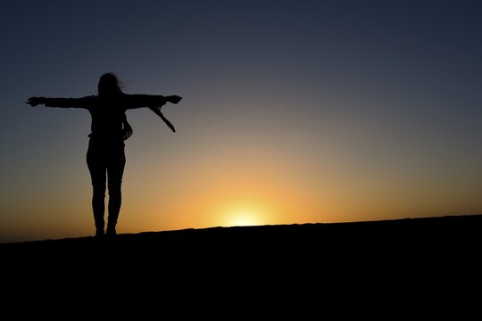 Standing woman in silouete with spreaded hands enjoying sunset on the dune. Morocco
