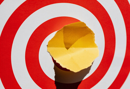 Red and white circular bullseye target torn paper center hole revealing bright yellow background studio lighting