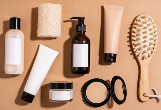 Skincare product bottles and bath accessories arranged on beige background with sharp shadows and blank mockup labels