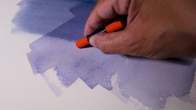 Hand drawing with an orange wax crayon over a watercolor wash on textured paper, adding expressive marks to a painted surface. Creative mixed media process for art, design and education.