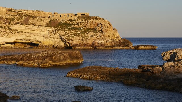 Evening light, calm sea, bay, Mare Morto, cliff, ruins of houses, rocks in the sea, Lampedusa Island, Agrigento Province, Pelagic Islands, Sicily, Italy