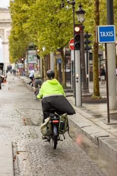 Cyclist riding through rainy Paris on the Champs-&Eacute;lys&eacute;es, with the Arc de Triomphe in the background, sustainable urban transportation