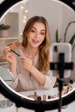 Beauty influencer filming makeup tutorial with smartphone ring light and eyeshadow palette at home