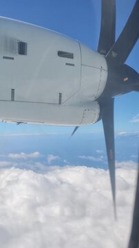 Primer plano en formato vertical del motor y las palas de la h&eacute;lice de un avi&oacute;n comercial turbopropulsor volando sobre un manto de nubes blancas y cielo azul.