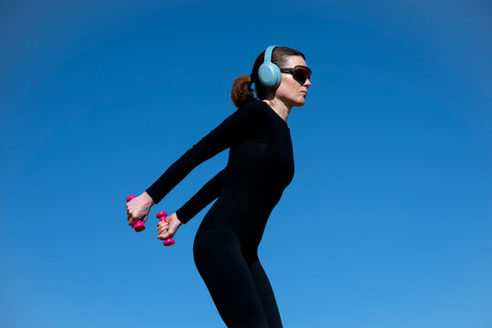 Woman Exercising with Dumbbells Against Clear Blue Sky