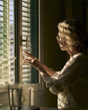 Middle aged woman closing exterior shutters to keep city apartment cool during a summer heatwave