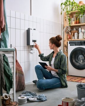 Homeowner checking wall mounted home battery system in utility room while managing everyday household energy use