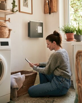 Homeowner checking wall mounted home battery system in utility room while managing everyday household energy use