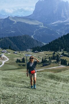 Woman shades her eyes on a grassy alpine trail below the Sassolungo massif. Solo hiking and mountain discovery for travel, sportswear and outdoor tourism marketing