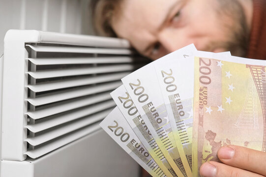 Human Hand Holding Euro Banknotes near Electric Heater Radiator at Home. Man Pay Money for Heating. Expensive to Heat. Energy Saving. Rising Cost of Living. Global Gas Crisis. Paying Cold Season Bills