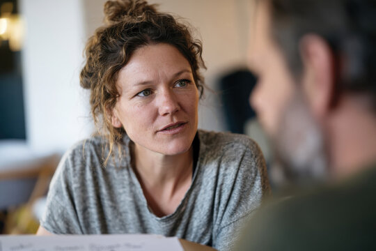 A woman with a messy bun displays a serious expression, reflecting deep emotion and engagement while having a serious discussion with a male friend at a table.