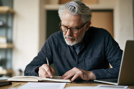 An older man is earnestly jotting down notes in a cozy and well-organized workspace, depicting the harmony between traditional skills and modern productivity.