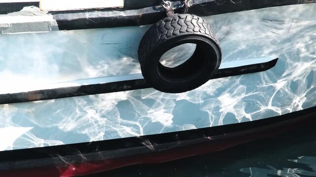 Sunlight caustics and water ripple reflection dancing on white boat hull with rubber tire fender