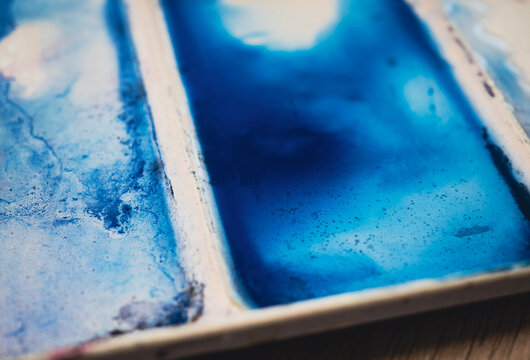 Blue watercolor paint and textured pigment in an artist palette, creating an abstract close up of fluid color, granulation and organic surface detail. Creative background for design projects.