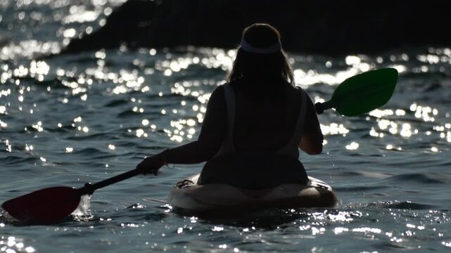 Kayaking woman paddling silhouette on sparkling ocean water during beautiful evening light adventure