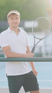 Tennis player poses with racket at a court in sunny weather