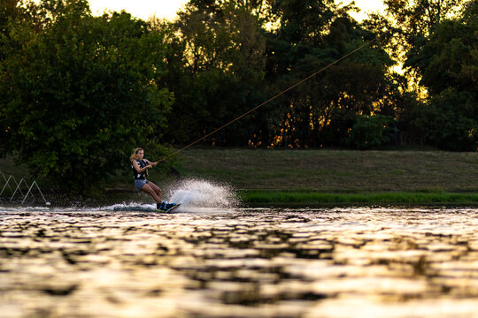 Female wakeboarder wakesurfing on sunset. Girl riding waterski cabel. Holding tow rope. Summer activities in the lake.