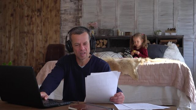 A man works remotely from home. Children play noisily. Tired sad stressed out father