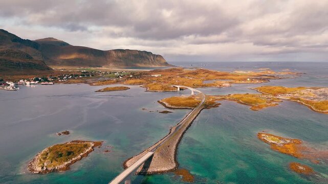 Aerial drone shot moving backward with slight pan left over coastal road and bridge in Norway with cars driving and scenic ocean landscape