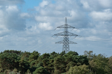 Obraz premium Electricity pylon stands tall among trees under blue sky with clouds