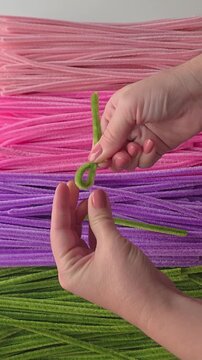 Hands shaping green chenille stem pipe cleaner craft close up top view