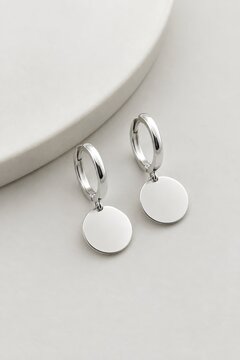 Minimalist silver hoop earrings with circular pendant dangles, elegant jewelry on neutral background, modern accessory design with reflective metallic finish, lifestyle product photography