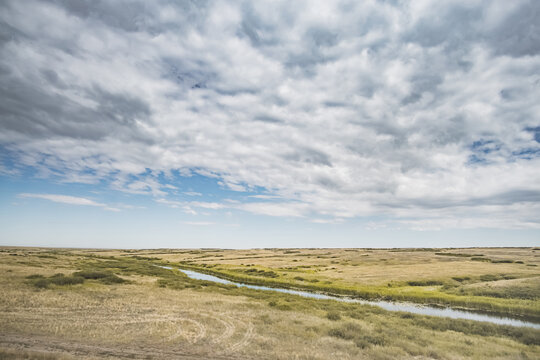 Steppe river flowing through the wild steppes of Kazakhstan in summer under cloudy skies; steppe landscape for background