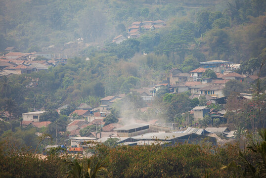 A residential neighborhood adjacent to lime processing plants in Citatah, West Bandung, Indonesia. Factory air pollution and dust linger over rooftops near heavily quarried limestone hills.