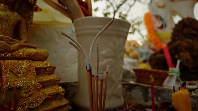 Burning Incense Sticks Stand Before Gold Religious Statues and Offerings at a Shrine, Showing Sacred Ritual and Spiritual Devotion