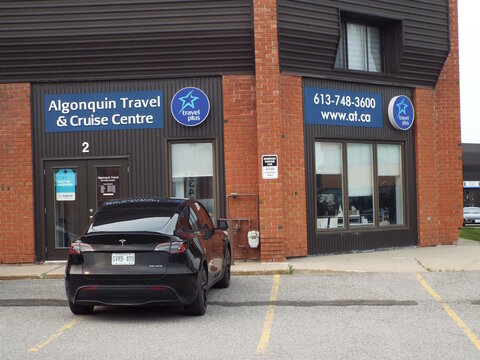 Ottawa, Ontario, Canada &ndash; July 19, 2026: A sign reading "Algonquin Travel and Cruise Centre" and "613-748-3600 www.at.ca" above unit 2 with parked dark Tesla at 5340 Canotek Rd.
