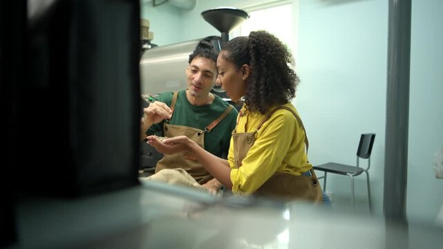 Two coffee professionals discussing and examining green coffee beans beside a commercial roasting machine during a quality assessment