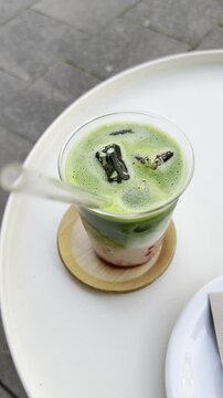 &Auml;sthetisches vertikales Reel: Sch&ouml;ner Iced Matcha mit Glasstrohhalm im Fokus in Nahaufnahme