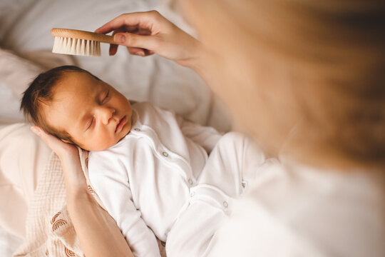 Woman holding sleeping baby boy brushing hair in bed close up top view. Motherhood.